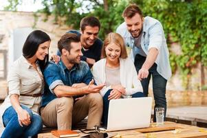 It is brilliant idea Group of joyful young people looking at laptop while working together outdoors photo