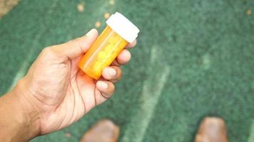 Adult left hand holds and turns an orange pill bottle with white tablets inside video