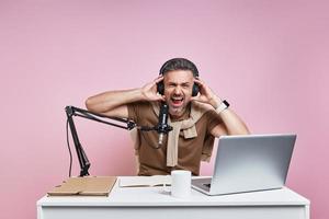 Excited man in headphones using microphone while recording podcast against pink background photo