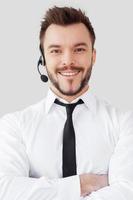 Confident male operator. Handsome young man in formalwear and headset looking at camera and smiling while standing against grey background photo