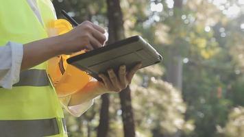 inteligente asiatico lavoratore uomo o maschio civile ingegnere con protettivo sicurezza casco e riflessivo veste utilizzando digitale tavoletta per progetto pianificazione e controllo architettonico disegno a costruzione luogo. video