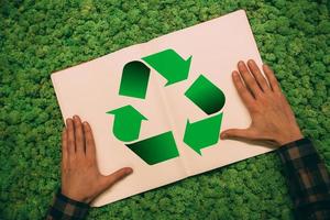 Think about future. Top view close-up image of man holding hands on his notebook with recycle symbol at moss background photo