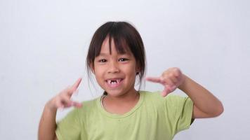 retrato de uma menina asiática com dentes de leite superiores quebrados e primeiros dentes permanentes. menina amigável mostrando seus dentes quebrados isolados no fundo branco. video