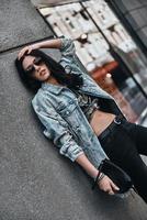 Feeling free to express herself. Beautiful young woman in denim jacket looking at camera while leaning on the building outdoors photo