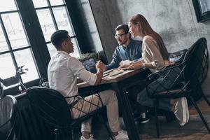 Group of young modern people in smart casual wear discussing something while working in office photo