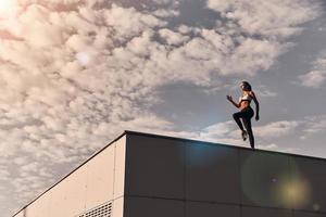 poder y belleza. toda la longitud de una joven moderna con ropa deportiva saltando mientras hace ejercicio en el techo al aire libre foto
