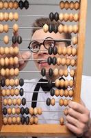 Nerd with abacus. Low angle view of excited young man in bow tie and suspenders holding abacus and calculating something while standing against grey background photo