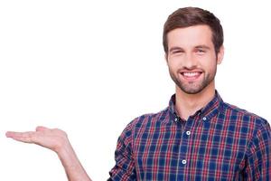 copie el espacio en su mano. retrato de un joven apuesto con un pantalones informal sosteniendo un espacio para copiar y mirando a la cámara con una sonrisa mientras se encuentra aislado en blanco foto