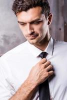 ajustando su corbata. apuesto joven en ropa formal ajustando su corbata y mirando hacia otro lado foto