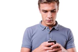 Checking incoming messages. Confident young man holding mobile phone and looking at it while standing isolated on white background photo