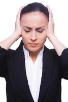 Stressed and overworked. Frustrated young woman in formalwear covering ears with hands and keeping eyes closed while standing isolated on white photo