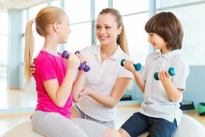 instructor con niños. instructor alegre que ayuda a los niños a hacer ejercicio en el club de salud foto