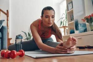 Flexible fit young woman in sports clothing stretching on exercise mat while spending time at home photo