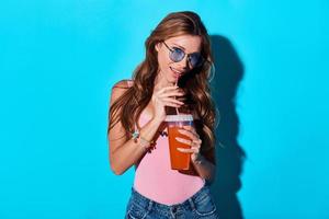 Cheerful beauty. Attractive young woman smiling and looking at camera while standing against blue background photo