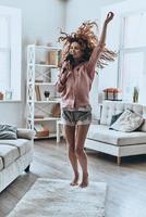 She is a star. Full length of attractive young women singing using comb and smiling while dancing at home photo