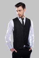 Confident in his perfect style. Handsome young man in formalwear holding hands in pockets and looking away while standing against grey background photo