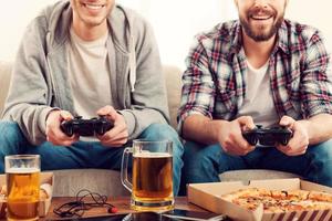 Time for games. Cropped image of two young men playing video games while sitting on sofa photo