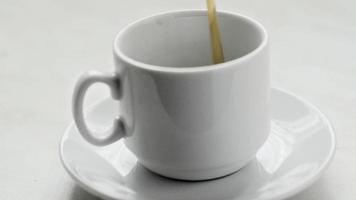 el café se vierte en una pequeña taza blanca sobre fondo blanco. mañana con café. video