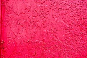 The texture of an iron metal painted bright red scarlet peeling paint old battered scratched cracked ancient rusty metal sheet wall with corrosion. The background photo