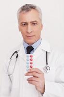 Take your pills Senior grey hair doctor in uniform holding pills at his hand and looking at camera while standing isolated on white photo