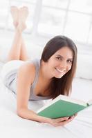 I love reading Beautiful young smiling woman lying in bed and reading a book photo