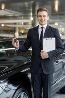 Good choice Handsome young classic car salesman standing at the dealership and holding a key photo