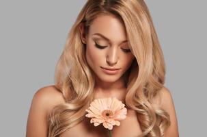 Sensual young woman enjoying her fresh flower while standing against grey background photo