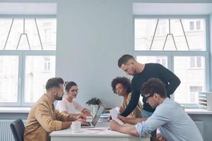 grupo de jóvenes confiados en ropa casual inteligente discutiendo negocios mientras se reúnen en la oficina foto