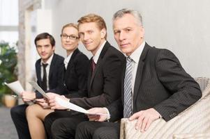 Waiting for job interview. Four people in formalwear waiting in line and smiling photo