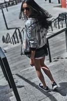 Great look. Full length rear view of beautiful young woman in casual wear looking over her shoulder while walking down the stairs outdoors photo