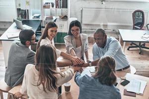 We are best team Top view of business colleagues holding hands on top of one another in a symbol of unity while working behind the glass wall in the board room photo