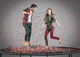 diversión colorida. toma en el aire de una hermosa pareja joven y alegre saltando en un trampolín junto con confetti a su alrededor foto