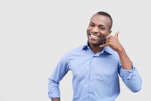 Call me Handsome young African man showing a call me sign and smiling while standing isolated on grey background photo