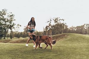 Full length of beautiful young woman playing with her dog and smiling while running outdoors photo