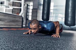 Giving all his best. Handsome young African man in sport clothing doing push-ups while exercising in the gym photo