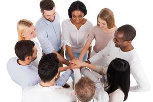 Proudly successful team. Top view of positive diverse group of people in smart casual wear keeping their hands clasped and smiling while standing close to each other photo