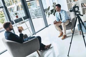 Business interview. Two young men in smart casual wear talking while making new video indoors photo