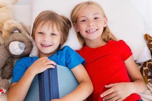 pequeños ratones de biblioteca. vista superior de dos lindos niños sosteniendo un libro mientras están acostados juntos en la cama foto