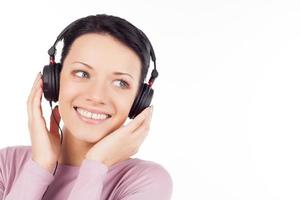 Listening to her favorite music. Beautiful young woman in headphones listening to the music and smiling while isolated on white photo