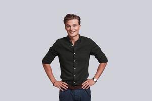 Young and successful. Good looking young man keeping hands on hips and looking at camera while standing against grey background photo