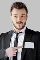 I am a big boss here. Young and bossy man in formalwear looking at camera and pointing his badge while standing against grey background photo