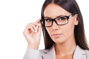 How may I help you Beautiful young businesswoman in suit adjusting her eyeglasses and looking at camera while standing against white background photo