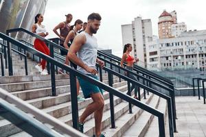 Group of young people in sports clothing jogging while exercising on the stairs outdoors photo