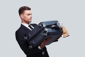 Difficult packing. Good looking young man carrying full suitcase while standing against grey background photo