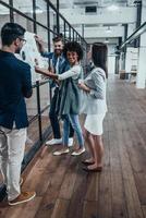 Searching for fresh ideas together. Full length of young modern people in smart casual wear planning business strategy while young woman pointing at large paper displayed on the glass wall in the office photo