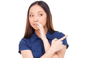 Telling hot gossips. Beautiful young Asian woman telling gossips and pointing away while standing isolated on white photo