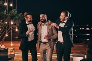 Three handsome men in suits drinking whiskey and communicating while spending time on party photo