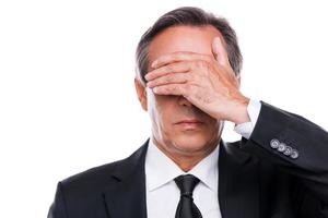 Feeling shame. Portrait of mature man in formalwear covering eyes with hand while standing against white background photo