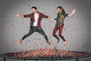 disfrutando de un tiempo divertido juntos. toma en el aire de una hermosa pareja joven y alegre tomándose de la mano mientras salta en el trampolín junto con confeti a su alrededor foto