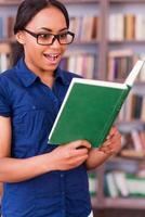 This book is so exciting Surprised African female student reading a book and keeping mouth open while standing in library photo